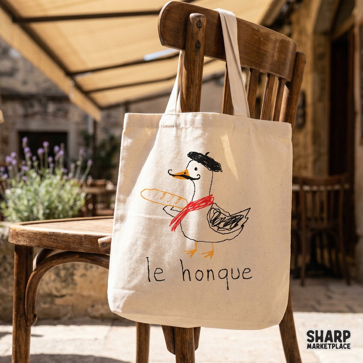 A tote bag featuring a hand-drawn goose wearing a beret and red scarf while holding a baguette, with the funny caption le honque printed below.