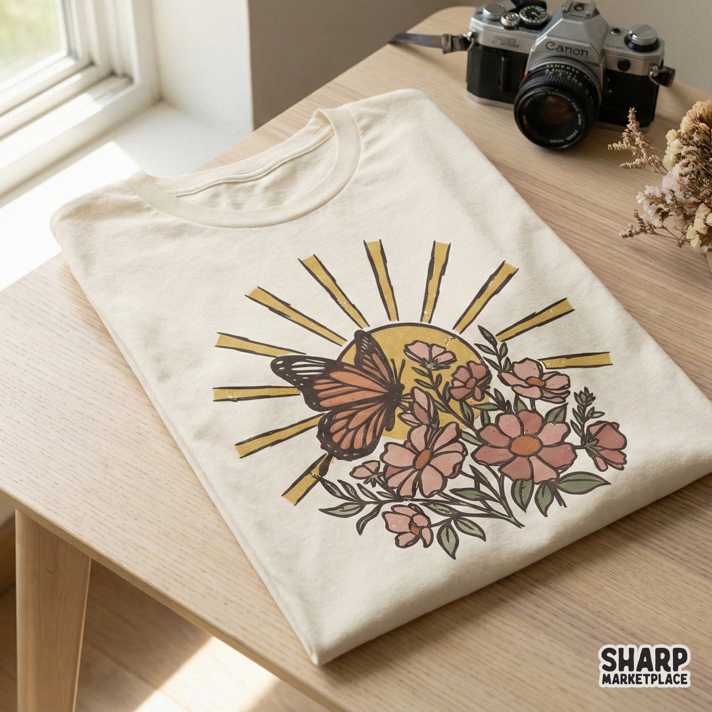 Vintage style butterfly resting on blooming flowers against a radiant sun, featured on a cream colored t-shirt for a boho aesthetic.