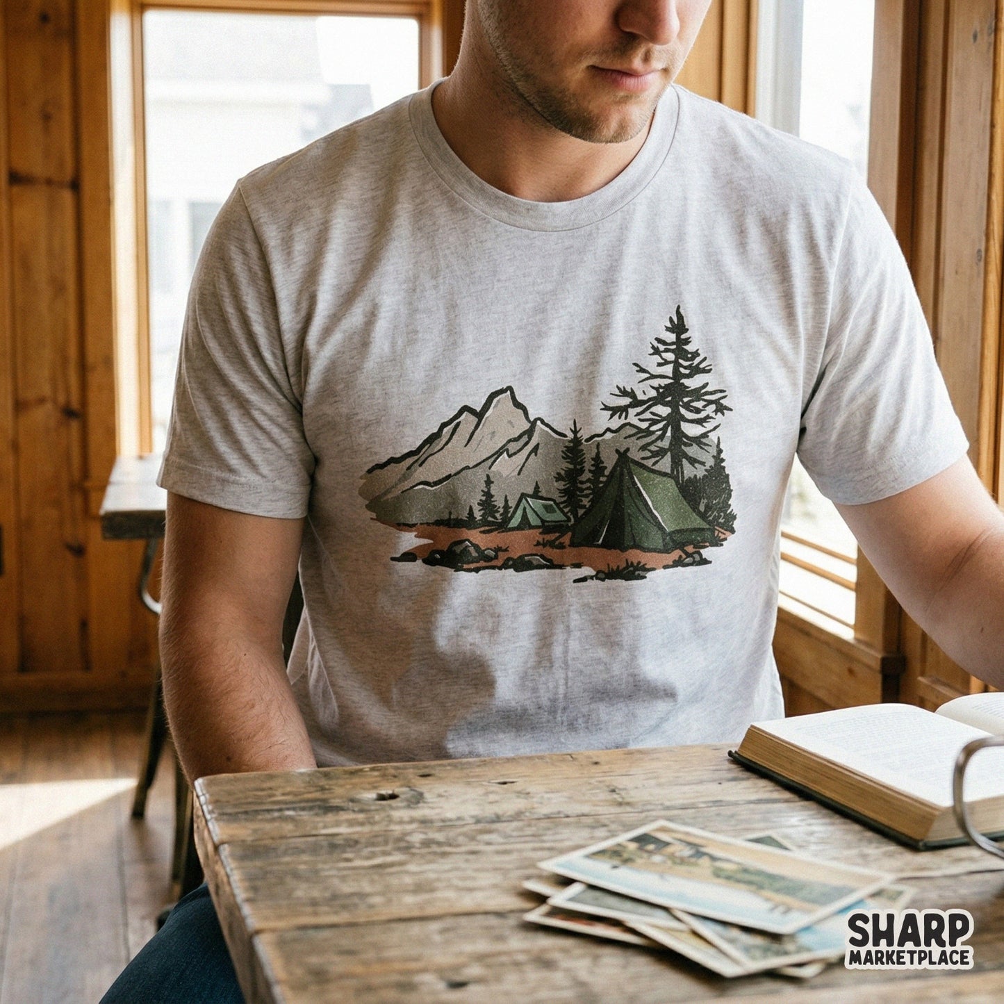 Retro outdoor adventure graphic printed on a light grey t-shirt, showcasing a hand-drawn forest tent, pine trees, and mountain peaks in muted colors.