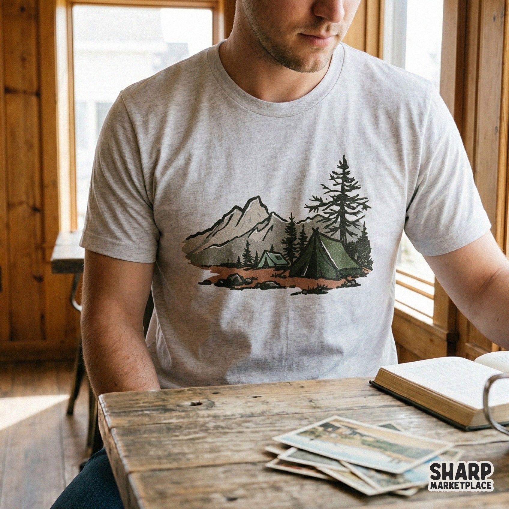 Retro outdoor adventure graphic printed on a light grey t-shirt, showcasing a hand-drawn forest tent, pine trees, and mountain peaks in muted colors.