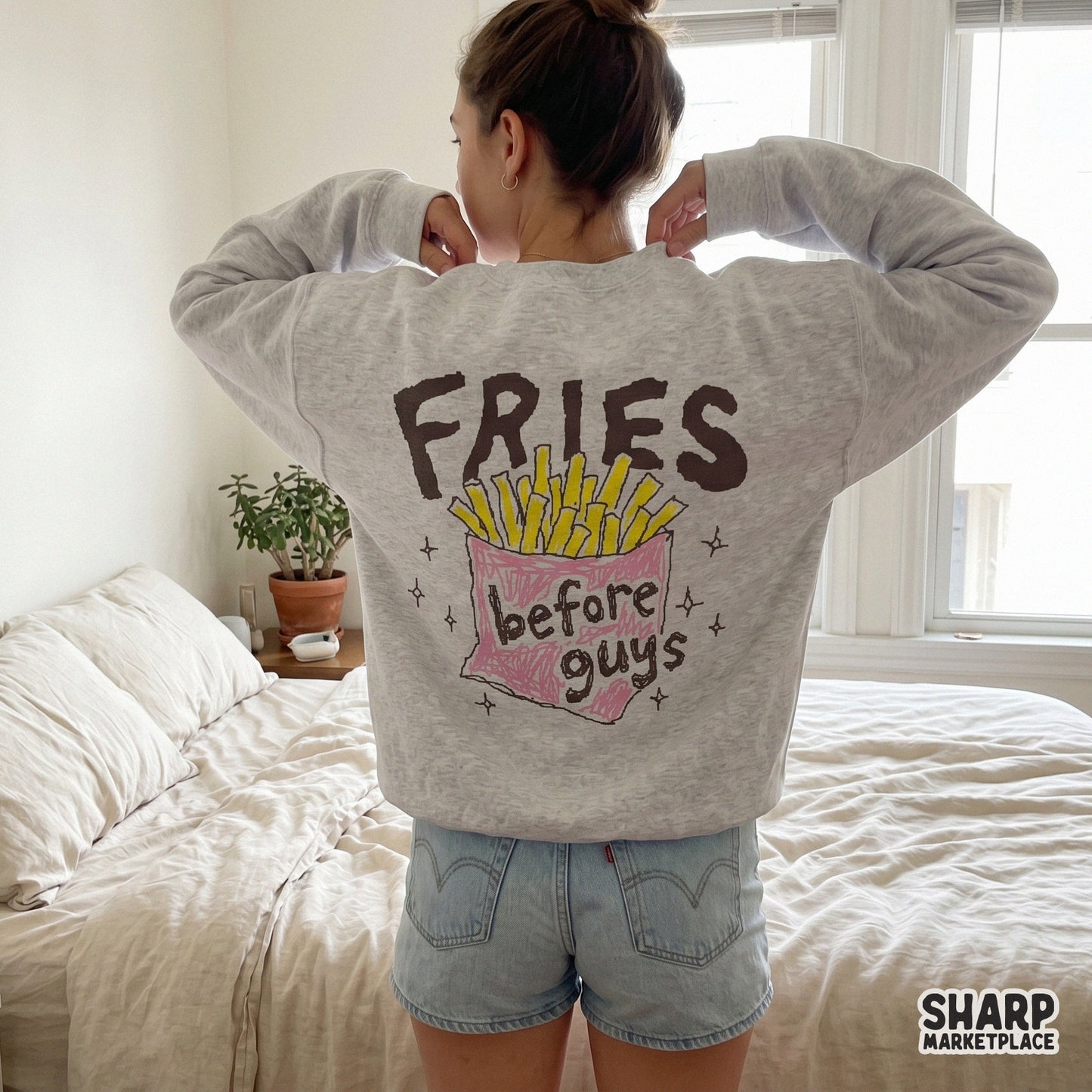 A grey sweatshirt worn from the back displaying a colorful crayon-style graphic of french fries in a pink carton with the quote Fries before guys.