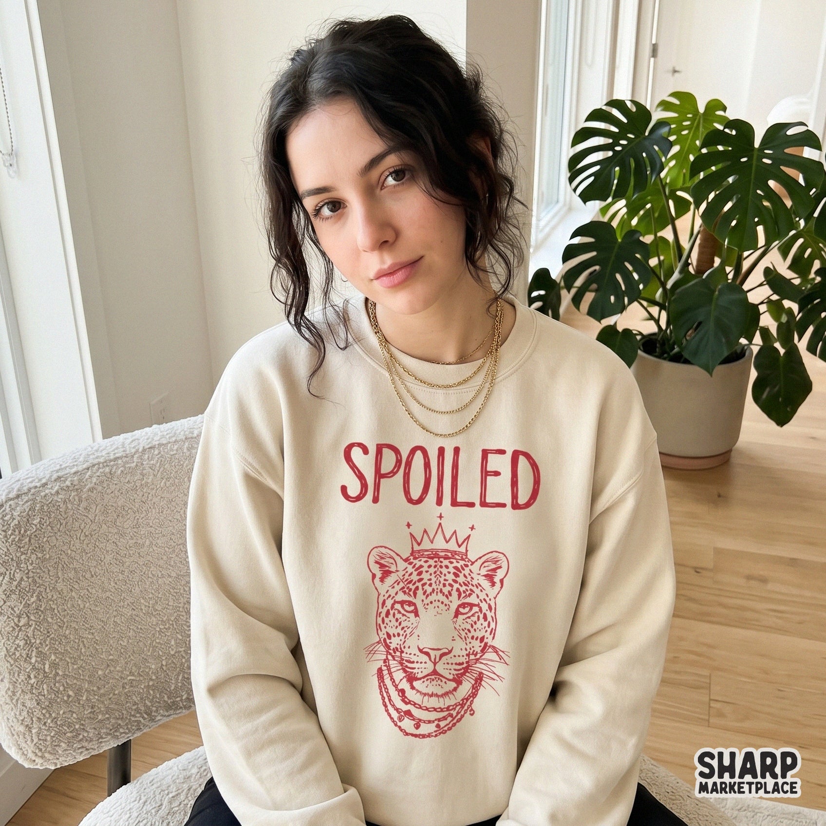 A digital design featuring a sassy leopard portrait in red ink with a crown and jewelry, shown printed on a neutral-colored sweatshirt for fashion.