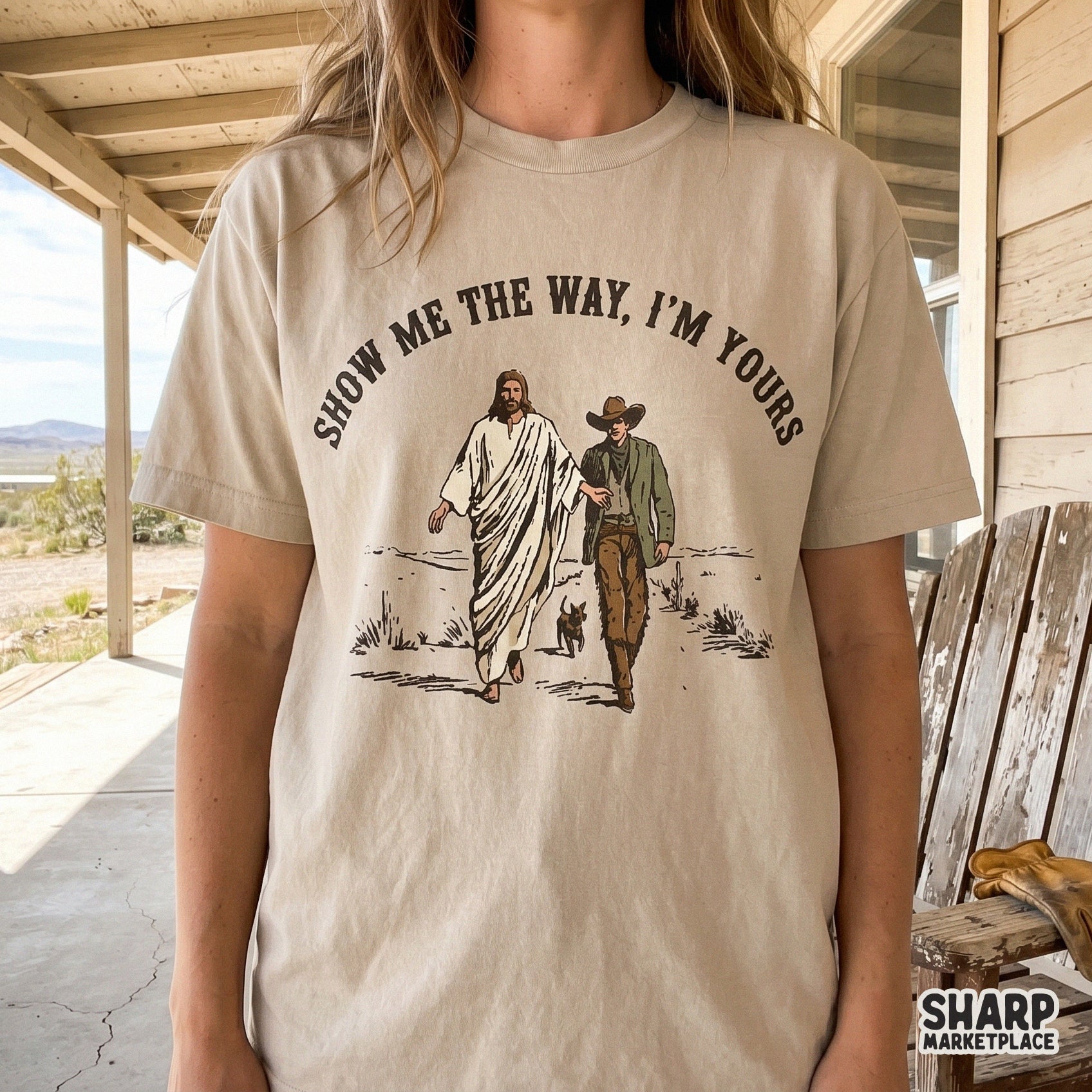 Sublimation design on a t-shirt showing a hand-drawn illustration of Jesus guiding a cowboy across a dusty path, rendered in muted earth tones.