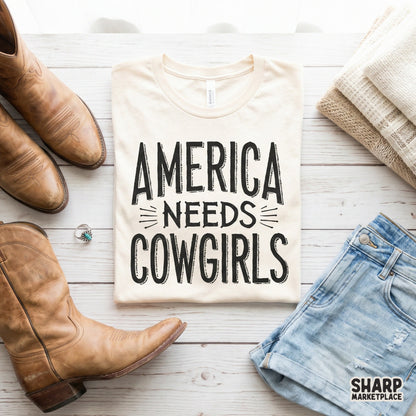 Vintage style western quote America Needs Cowgirls in a bold hand-drawn font, suitable for DTF printing on country-themed shirts and rodeo gear.