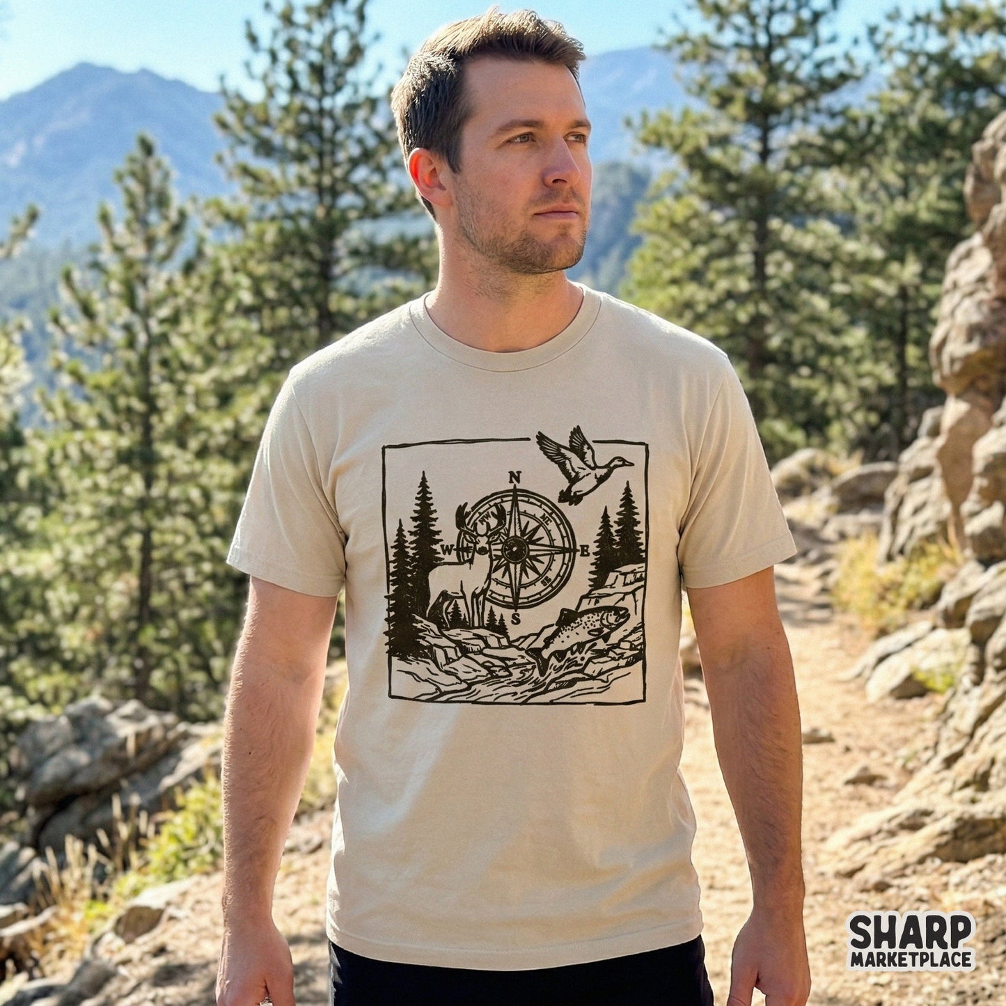 Rustic woodblock-style outdoor graphic printed on a beige t-shirt, showcasing a compass, whitetail deer, mallard duck, and trout for nature lovers.