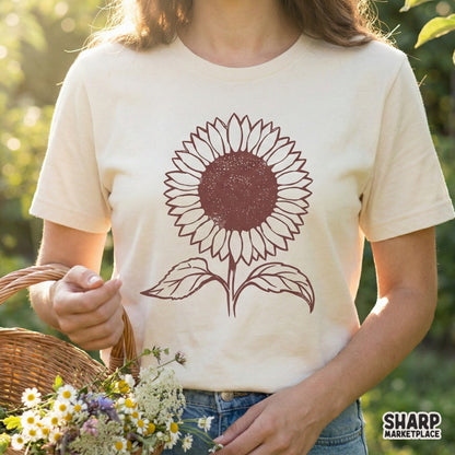 Muted maroon sunflower botanical graphic with rustic textured center and symmetrical leaves, displayed as a digital design on a cream t-shirt.