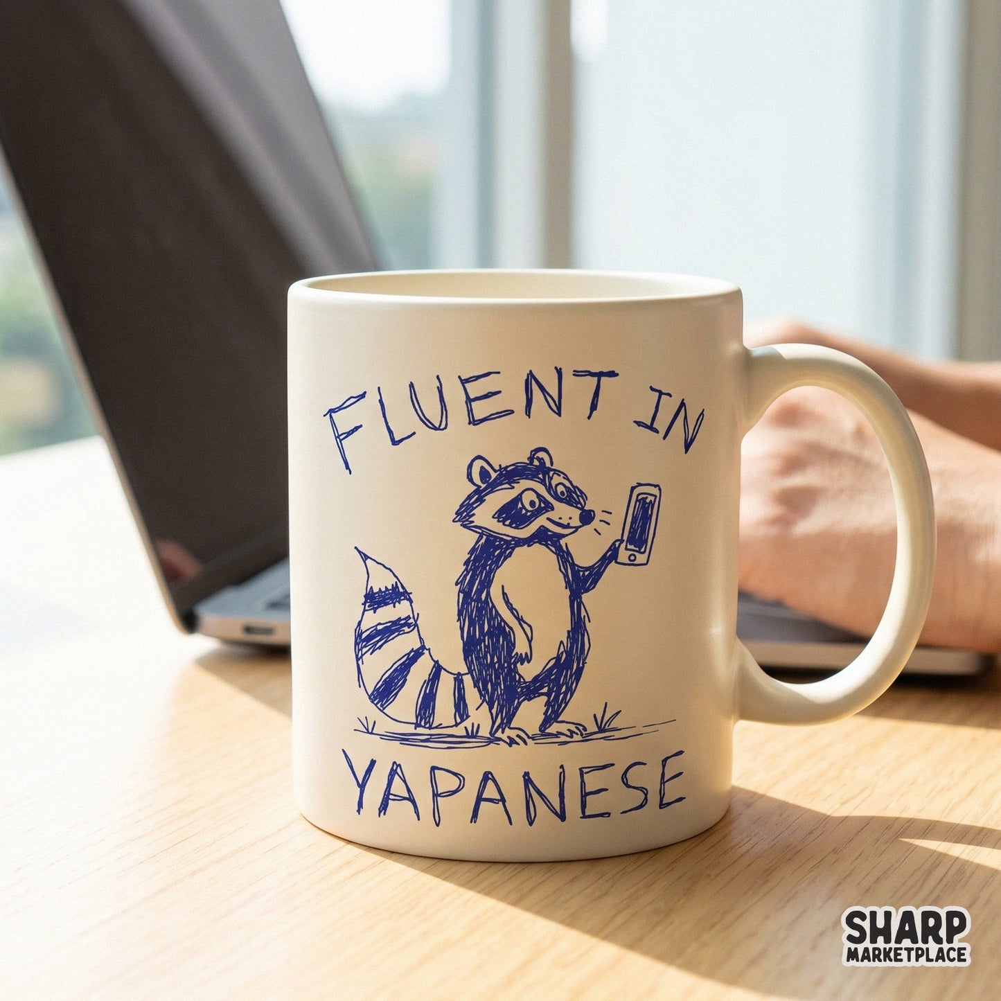 A white ceramic mug featuring a blue ink sketch of a raccoon looking at a phone with the funny phrase Fluent In Yapanese printed above and below.
