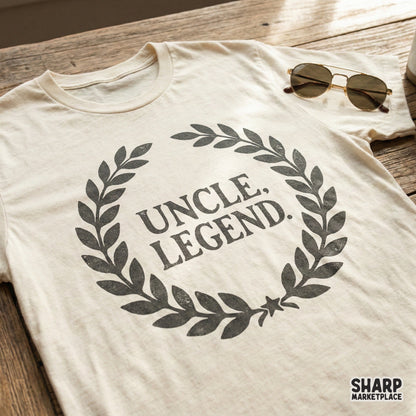 Distressed black Uncle Legend text framed by a classic laurel wreath on a cream t-shirt mockup, ideal for masculine gifts and retro style clothing.
