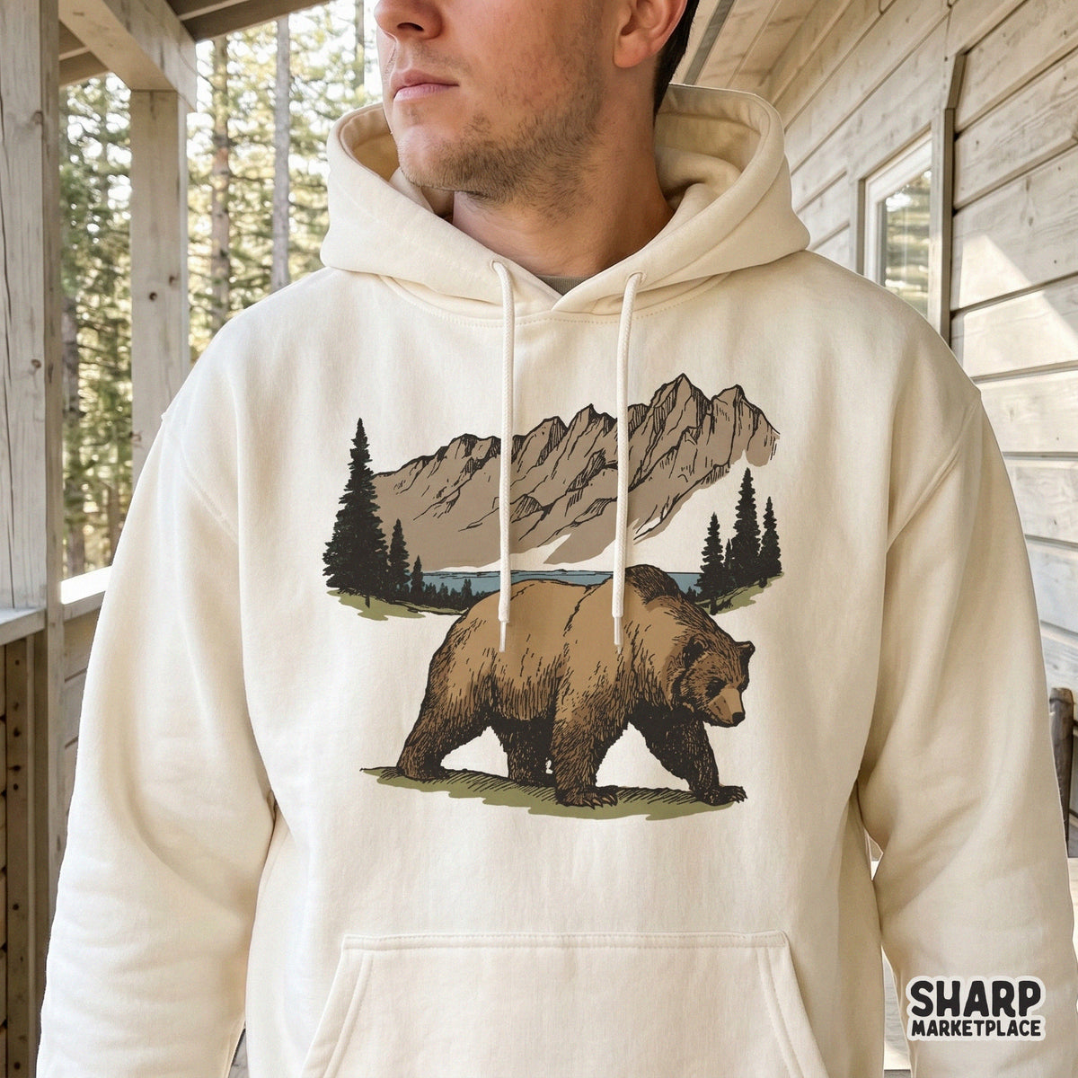 Detailed grizzly bear mountain scene design printed on a cream hoodie, featuring a rustic forest and lake illustration for nature-themed apparel.