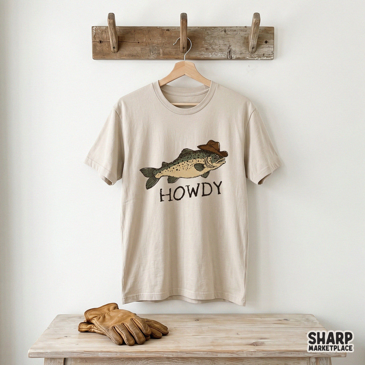 A beige t-shirt featuring a hand-drawn illustration of a trout in a western hat with the text Howdy, perfect for fishing-themed apparel designs.