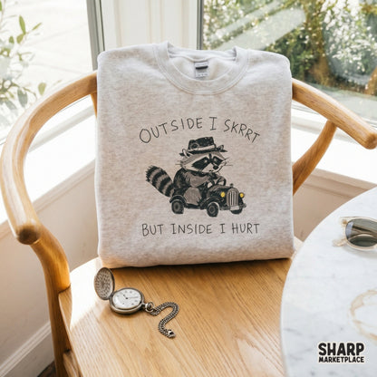 Whimsical raccoon car illustration with the sarcastic text Outside I Skrrt But Inside I Hurt, a high-resolution transparent PNG for DIY print projects.