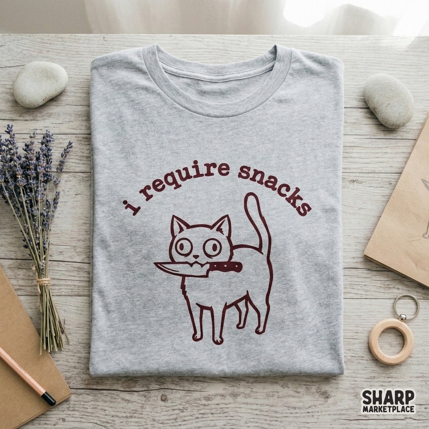 Digital graphic of a quirky cat holding a kitchen knife with the sarcastic phrase I require snacks in bold red lettering, perfect for sublimation designs.