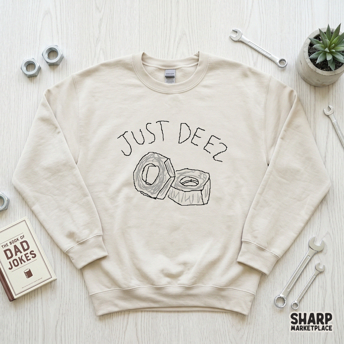 Beige crewneck sweatshirt featuring a minimalist hand-drawn illustration of two hardware nuts and the playful text Just Deez for a sarcastic look.