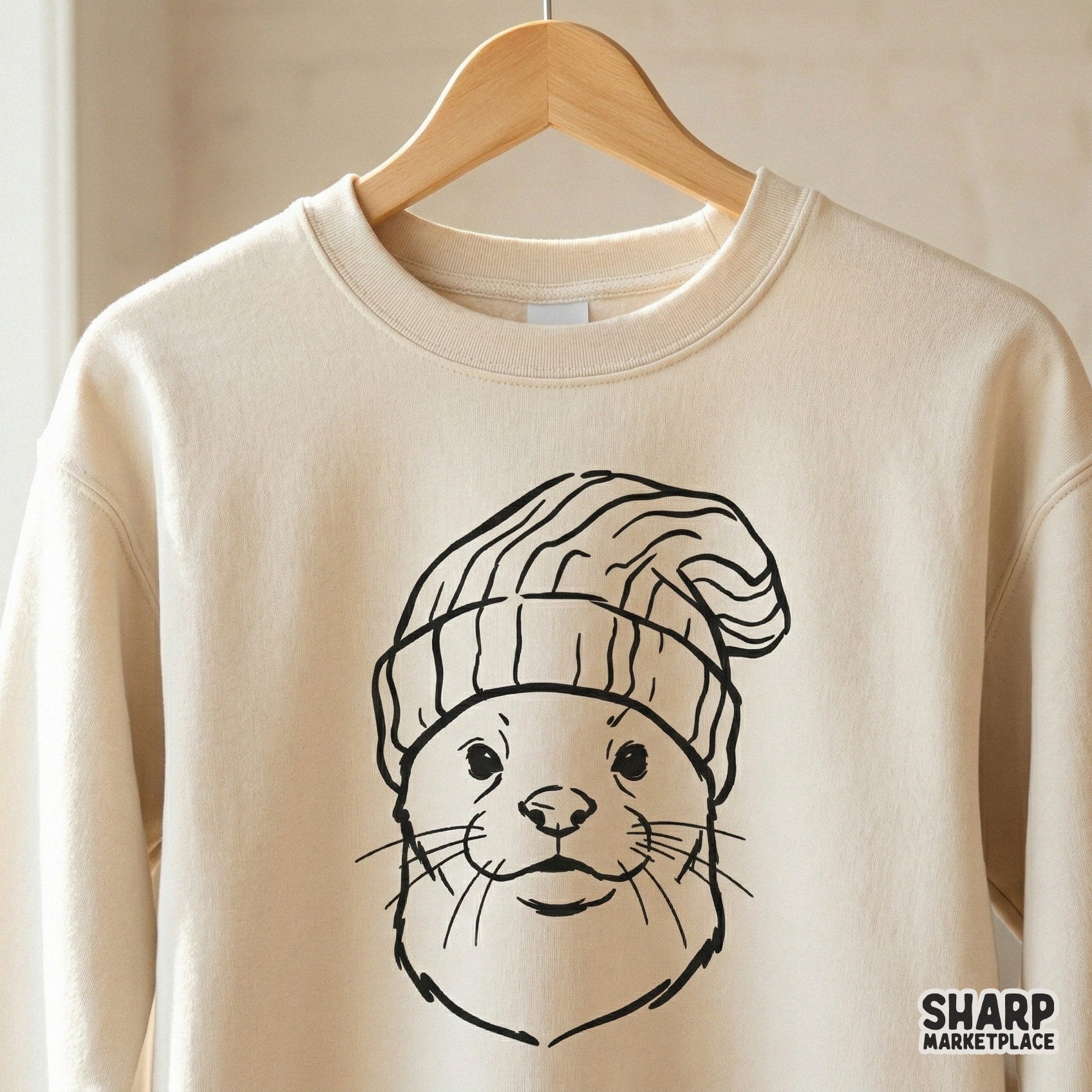 A clean black line drawing of an otter in a winter hat displayed on a cream-colored sweatshirt mockup, ideal for custom clothing and DIY gifts.