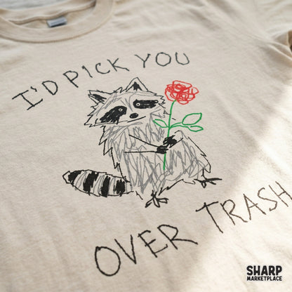 Close-up of a t-shirt design featuring a scribbled raccoon holding a red rose with the funny text I'd Pick You Over Trash for apparel sublimation.
