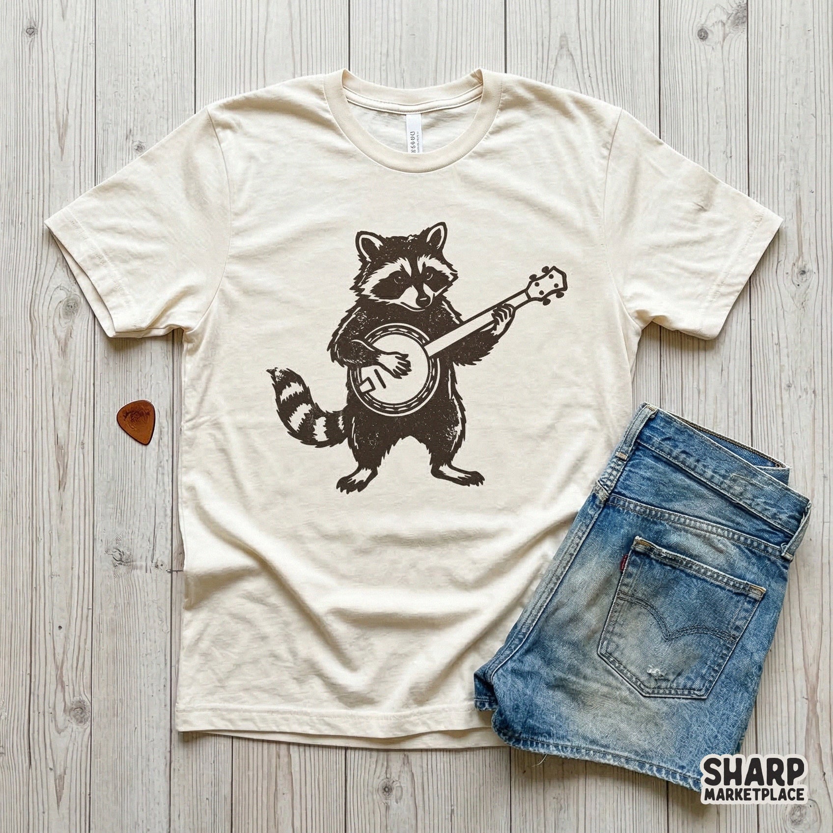 Apparel mockup showcasing a dark brown raccoon playing a banjo design printed on a cream-colored t-shirt, perfect for folk music themed clothing.