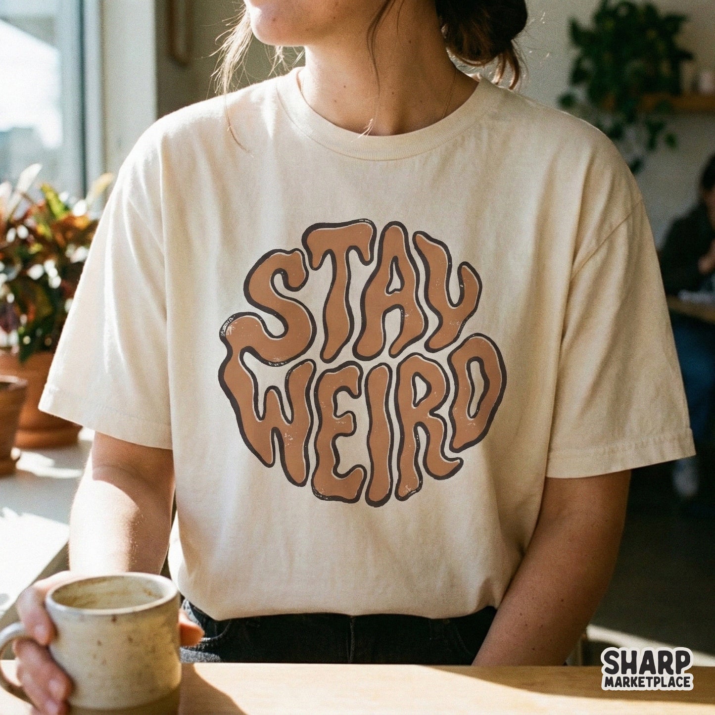 A mockup of a cream-colored t-shirt displaying the Stay Weird retro wavy text design in brown, perfect for trendy apparel and sublimation projects.