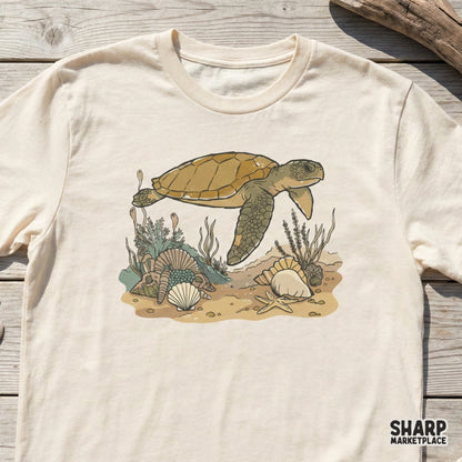Vintage-style sea turtle illustration printed on a cream-colored t-shirt, featuring a detailed underwater scene with shells and marine plants.