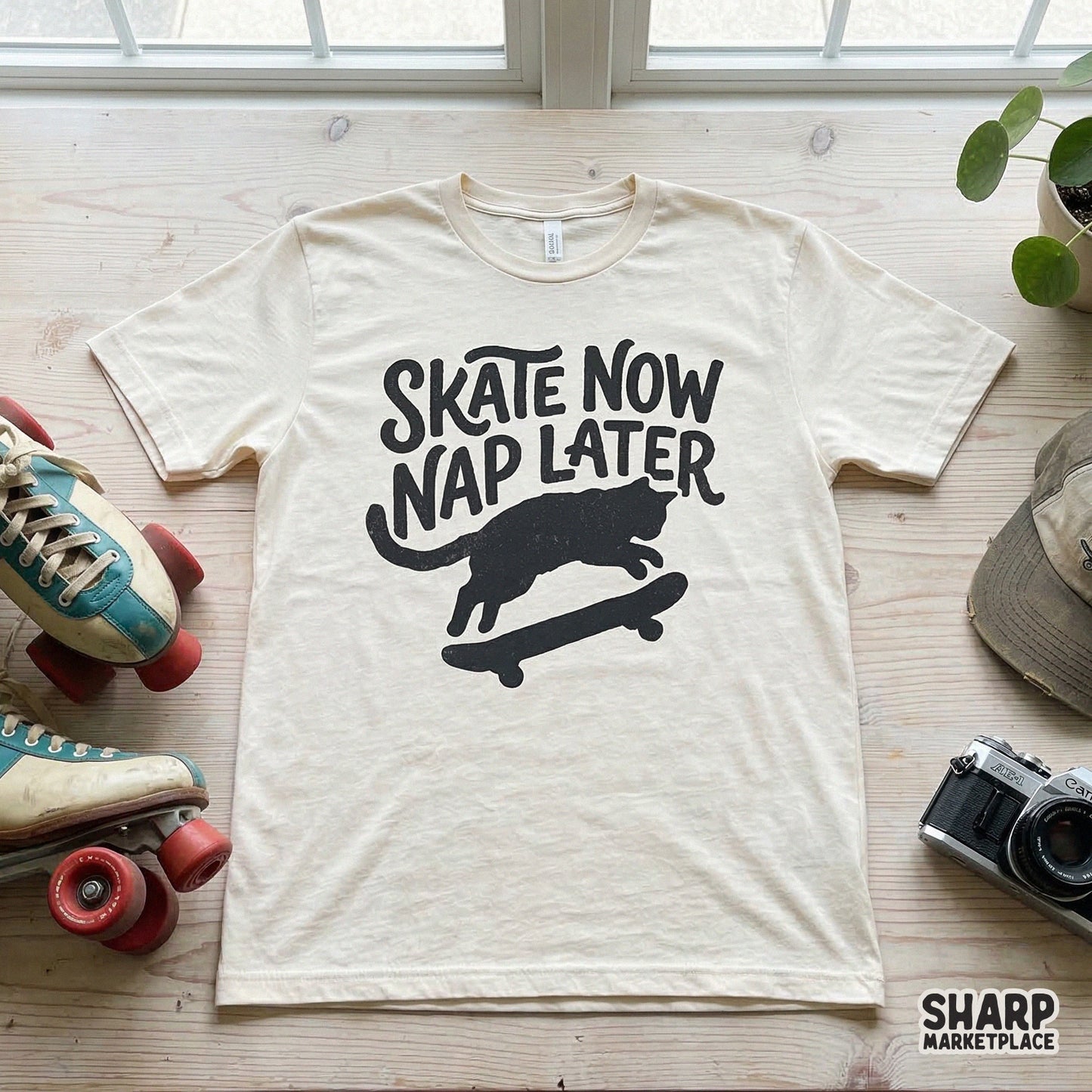 Cream colored t-shirt featuring a playful black silhouette of a cat skateboarding with the quote Skate Now Nap Later in a trendy, distressed font.
