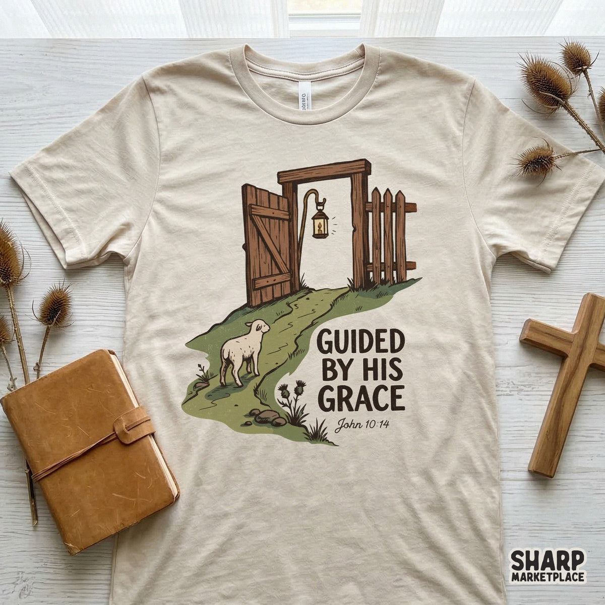 Faith-based apparel design on a beige t-shirt showing a hand-drawn lamb, a wooden gate, and the inspirational quote Guided By His Grace in earth tones.
