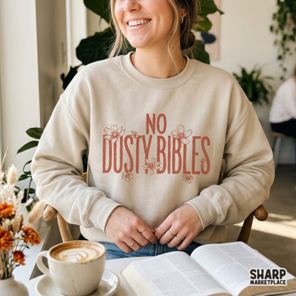 A neutral-colored sweatshirt featuring the No Dusty Bibles quote in rust-colored typography accented with floral line art for a faith-based look.