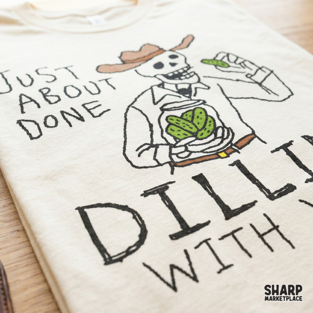 Western-themed digital design of a skeleton cowboy eating a pickle with the funny quote Just About Done Dillin With Yall for custom apparel.