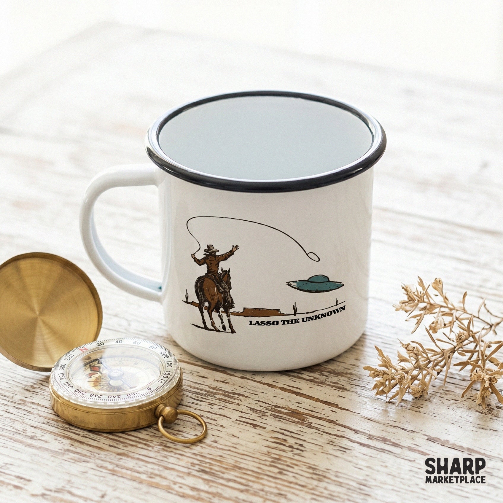 Vintage style sublimation design showing a cowboy roping a UFO in a desert, displayed on a white enamel camping mug.