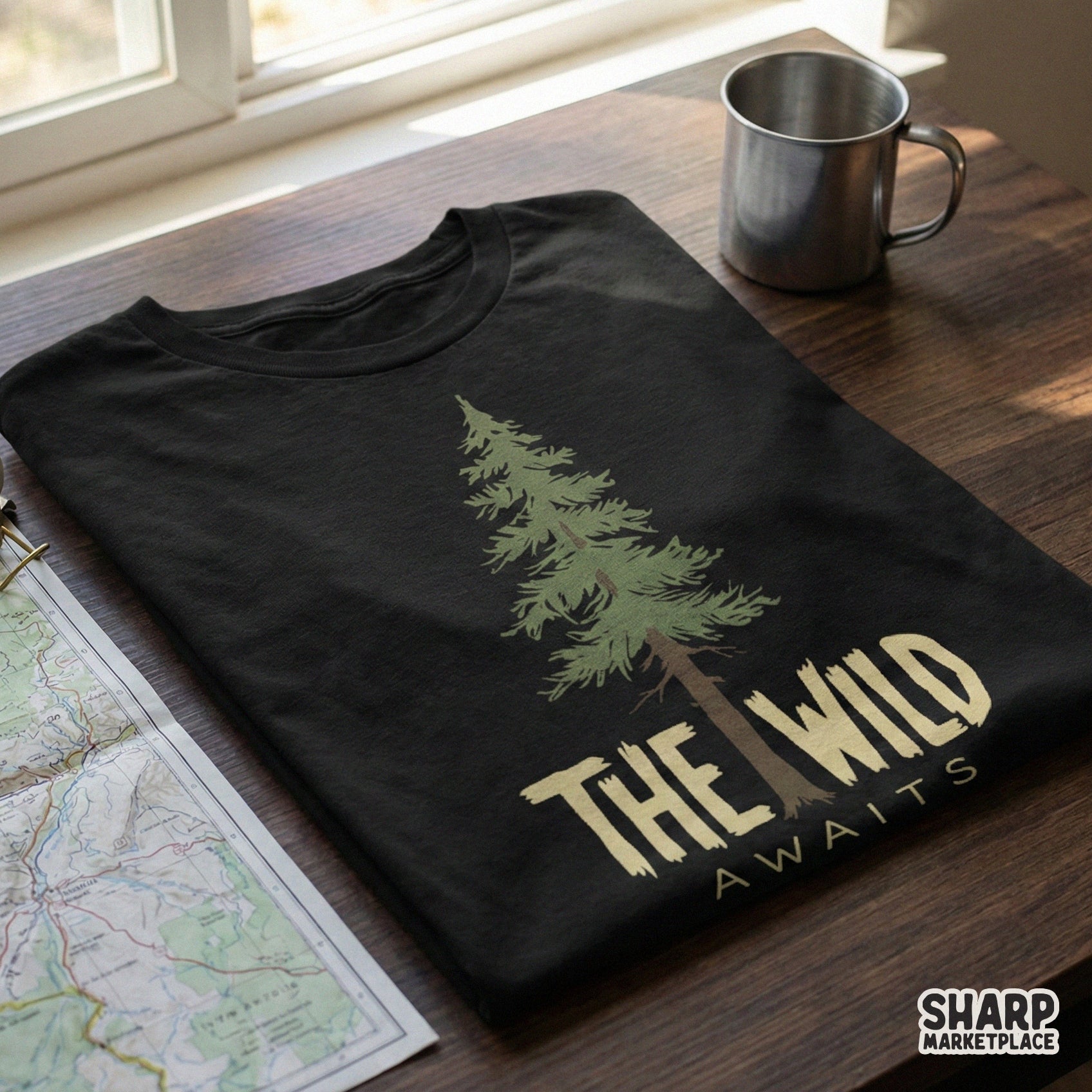 Black t-shirt featuring a detailed evergreen tree graphic and the rugged text The Wild Awaits, ideal for outdoor adventure and camping gear.
