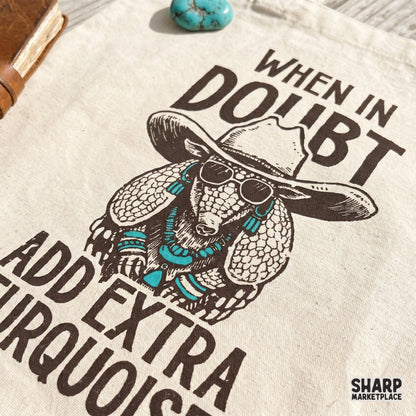 Distressed western armadillo graphic featuring turquoise jewelry and a cowboy hat, printed on a fabric tote bag for a boho desert aesthetic.