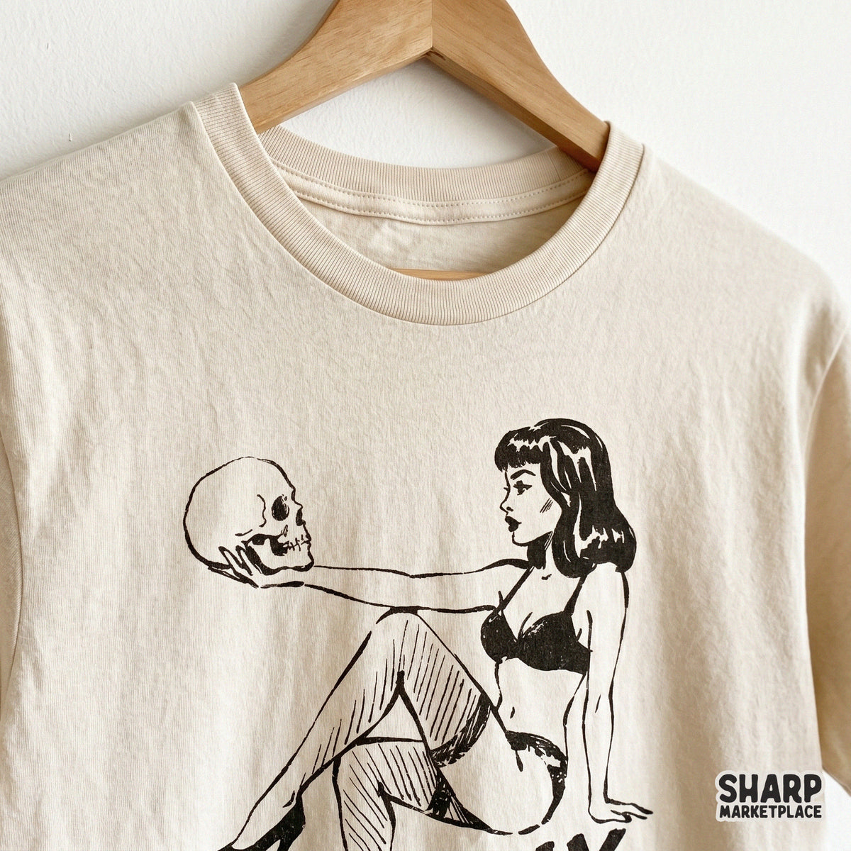 Distressed black ink illustration of a pinup girl gazing at a skull printed on a neutral t-shirt for horror-themed apparel and sublimation.