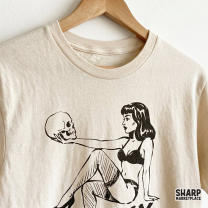 Distressed black ink illustration of a pinup girl gazing at a skull printed on a neutral t-shirt for horror-themed apparel and sublimation.
