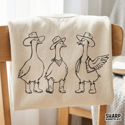 Vintage-inspired illustration of a silly goose trio in western attire, featuring cowboy hats, a bandana, and a vest, printed on a neutral shirt.