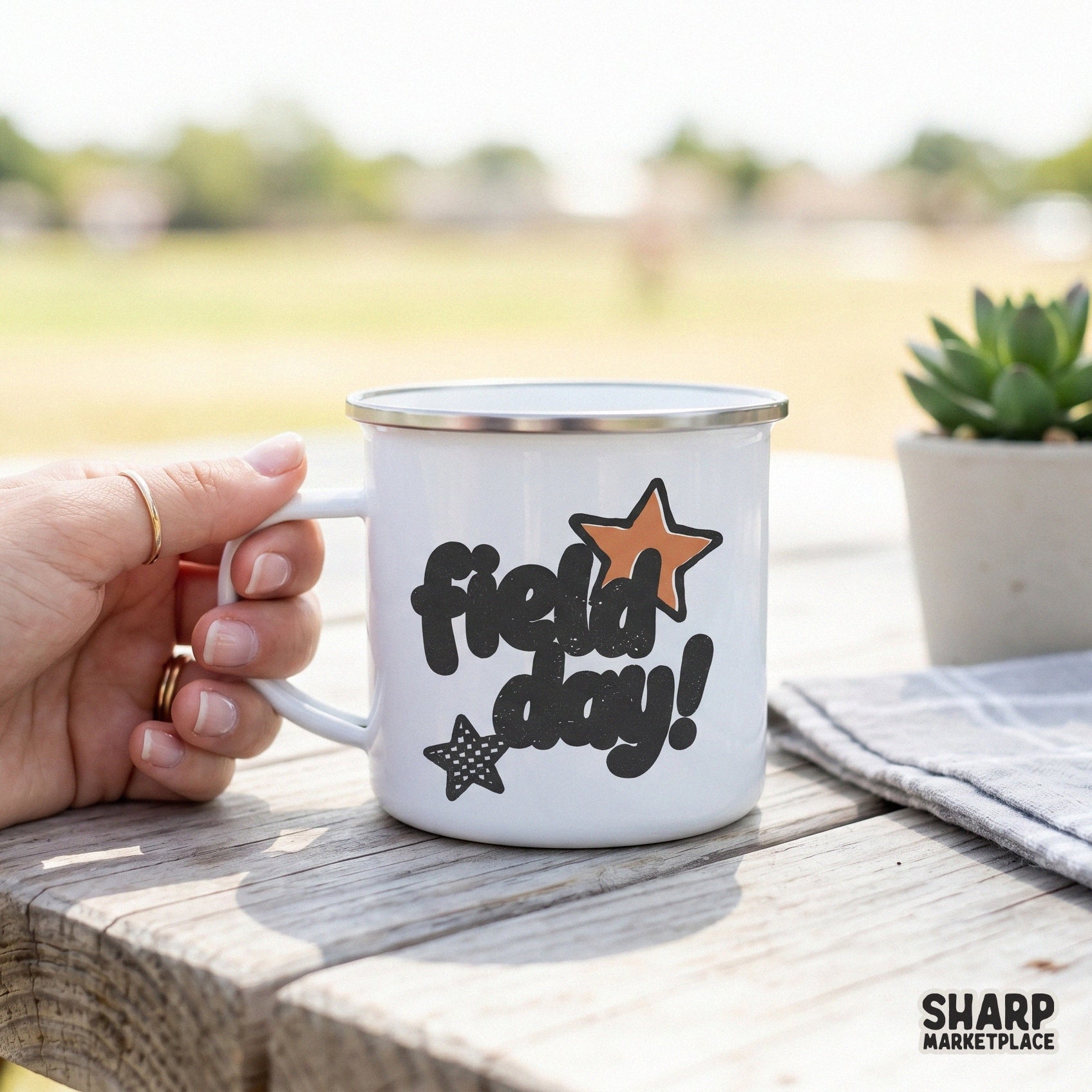 White enamel mug mockup displaying a retro Field Day graphic with distressed charcoal bubble text and orange star accents for school event apparel.