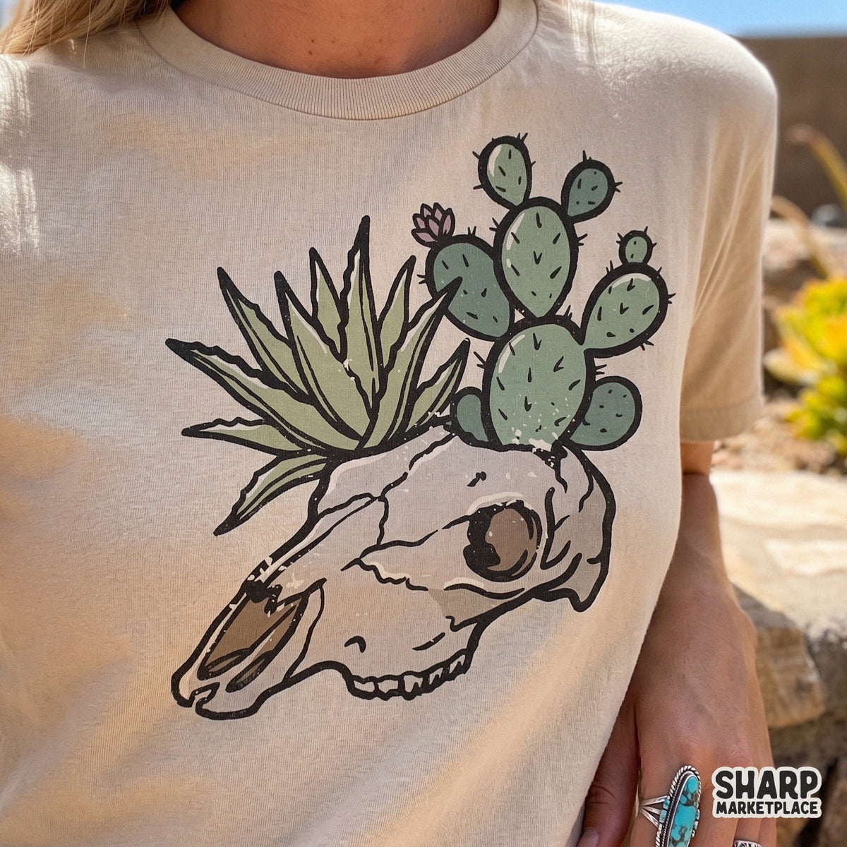 Trendy western boho graphic of a cow skull with desert plants printed on a beige t-shirt, perfect for sublimation, DTF transfers, and custom apparel.