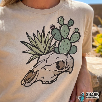 Trendy western boho graphic of a cow skull with desert plants printed on a beige t-shirt, perfect for sublimation, DTF transfers, and custom apparel.