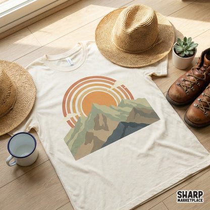 Vintage inspired mountain sunset graphic printed on a cream t-shirt, showcasing muted olive, tan, and blue peaks with retro sun rays.