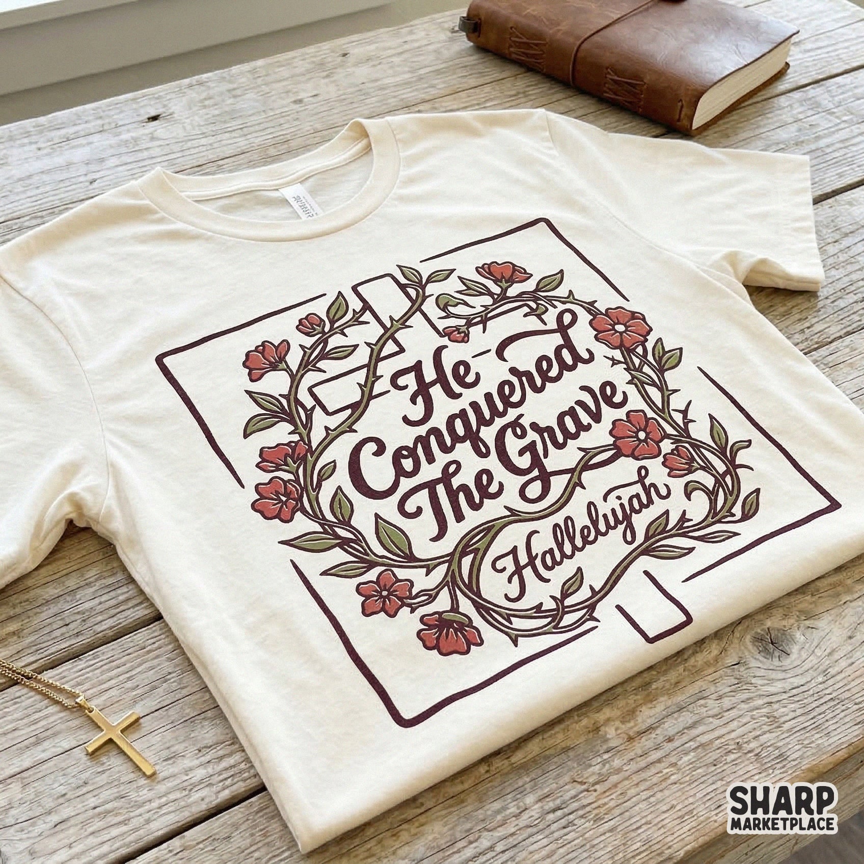 He Conquered The Grave Christian sublimation design printed on a cream t-shirt, featuring a floral cross and religious script in maroon tones.