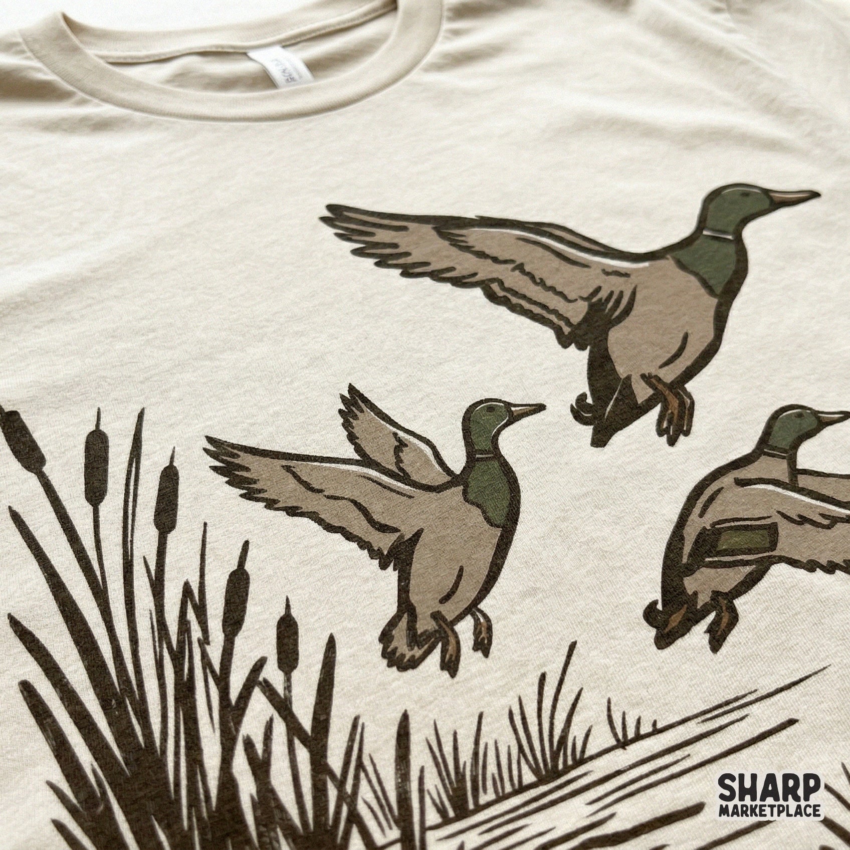 Close-up of a rustic mallard duck trio design printed on a light-colored t-shirt, showcasing the detailed hand-drawn marsh scene for sublimation.