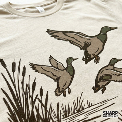 Close-up of a rustic mallard duck trio design printed on a light-colored t-shirt, showcasing the detailed hand-drawn marsh scene for sublimation.