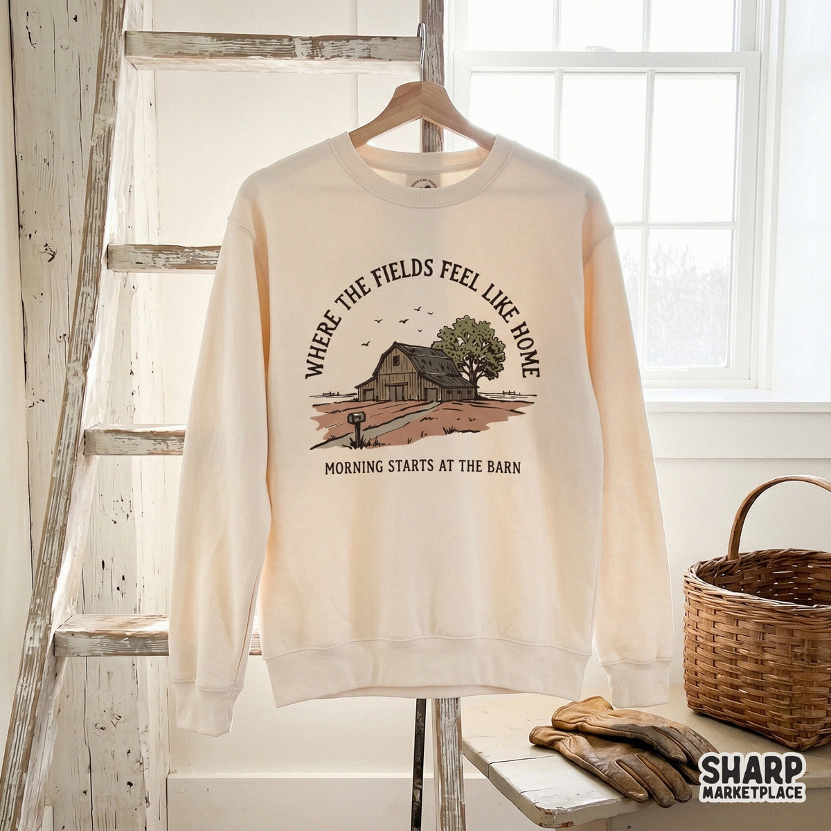 Cream-colored sweatshirt featuring a vintage-style barn illustration with the quote Where the Fields Feel Like Home and Morning Starts at the Barn.