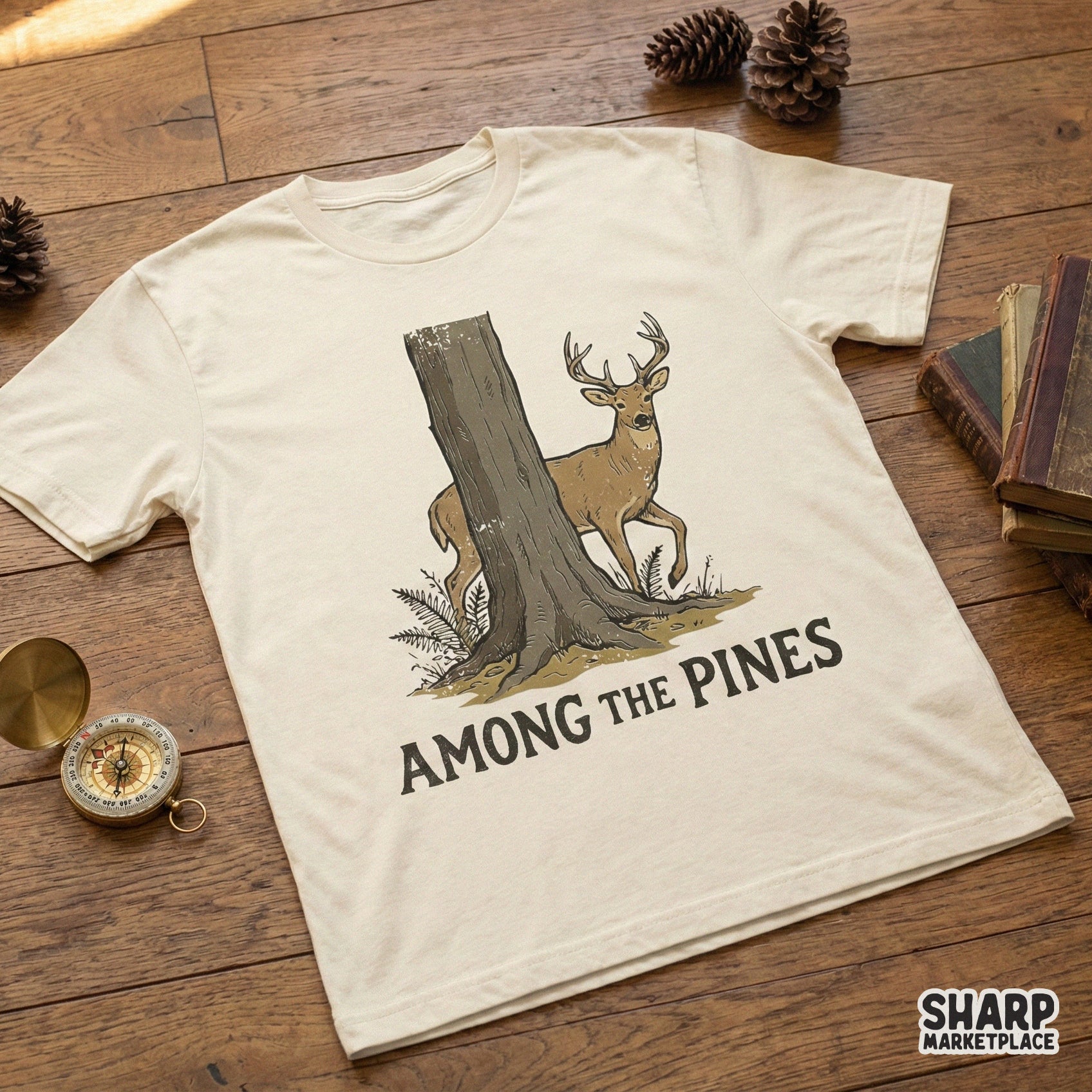 A cream colored t-shirt featuring a rustic deer and forest graphic with the words Among The Pines, perfect for outdoor themed apparel and sublimation.