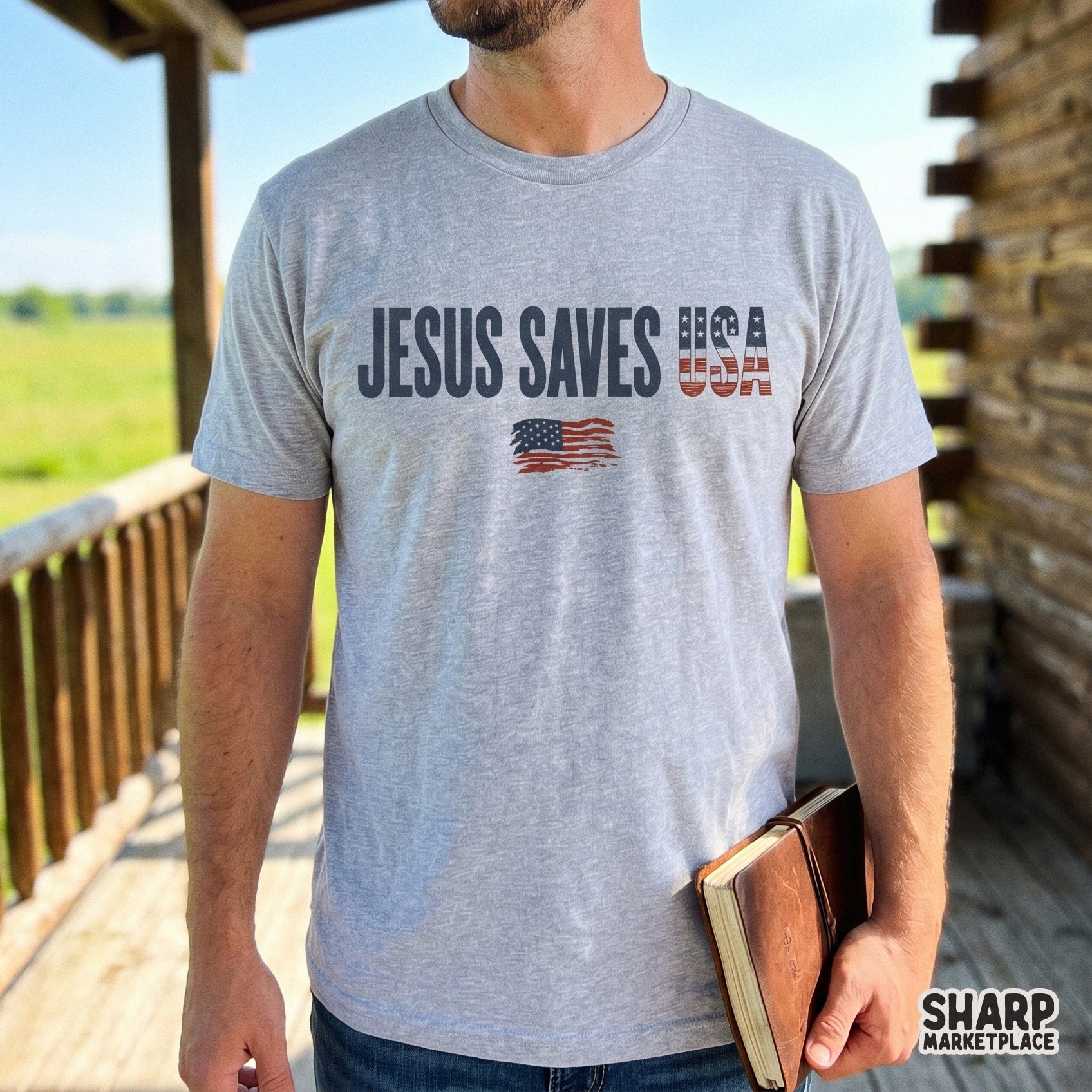 A gray t-shirt featuring the Jesus Saves USA text design with a patriotic flag pattern and a waving flag graphic centered on the chest.