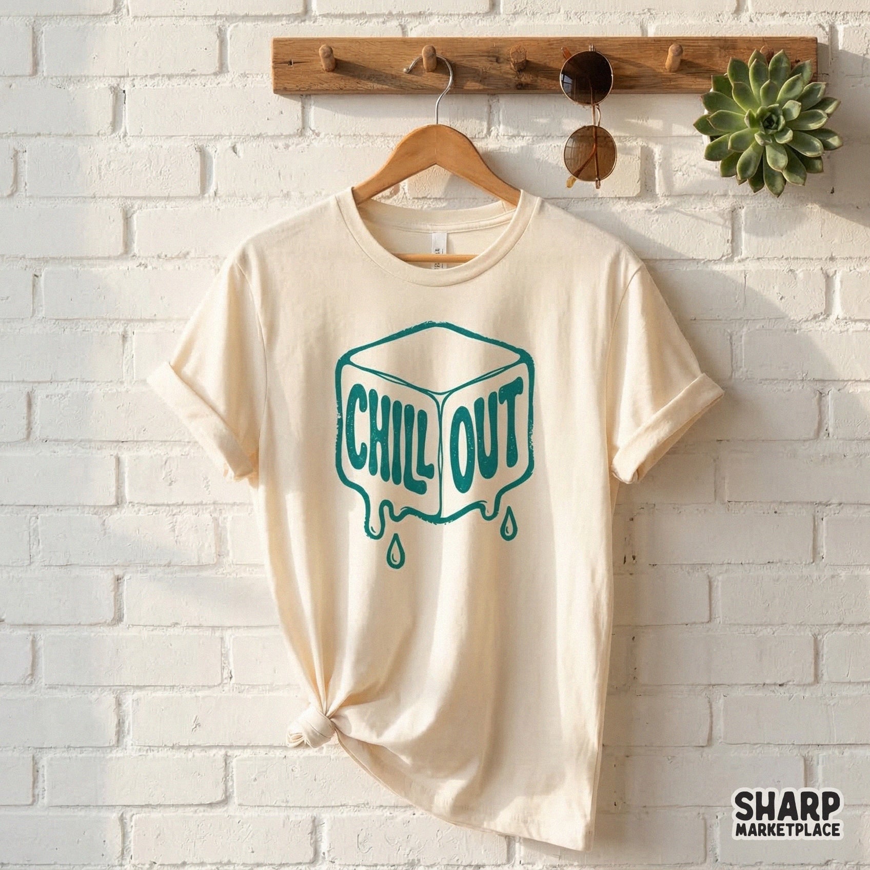 A cream colored t-shirt featuring a teal melting ice cube design with the words Chill Out in a playful, retro bubble font for summer projects.