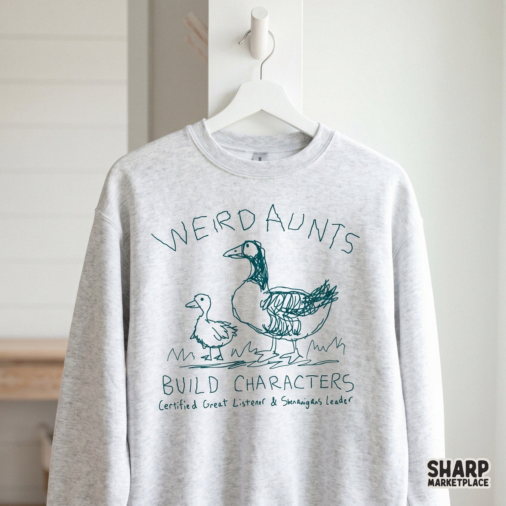 A light gray sweatshirt featuring a teal sketch of a goose and duckling with the humorous quote Weird Aunts Build Characters for apparel printing.