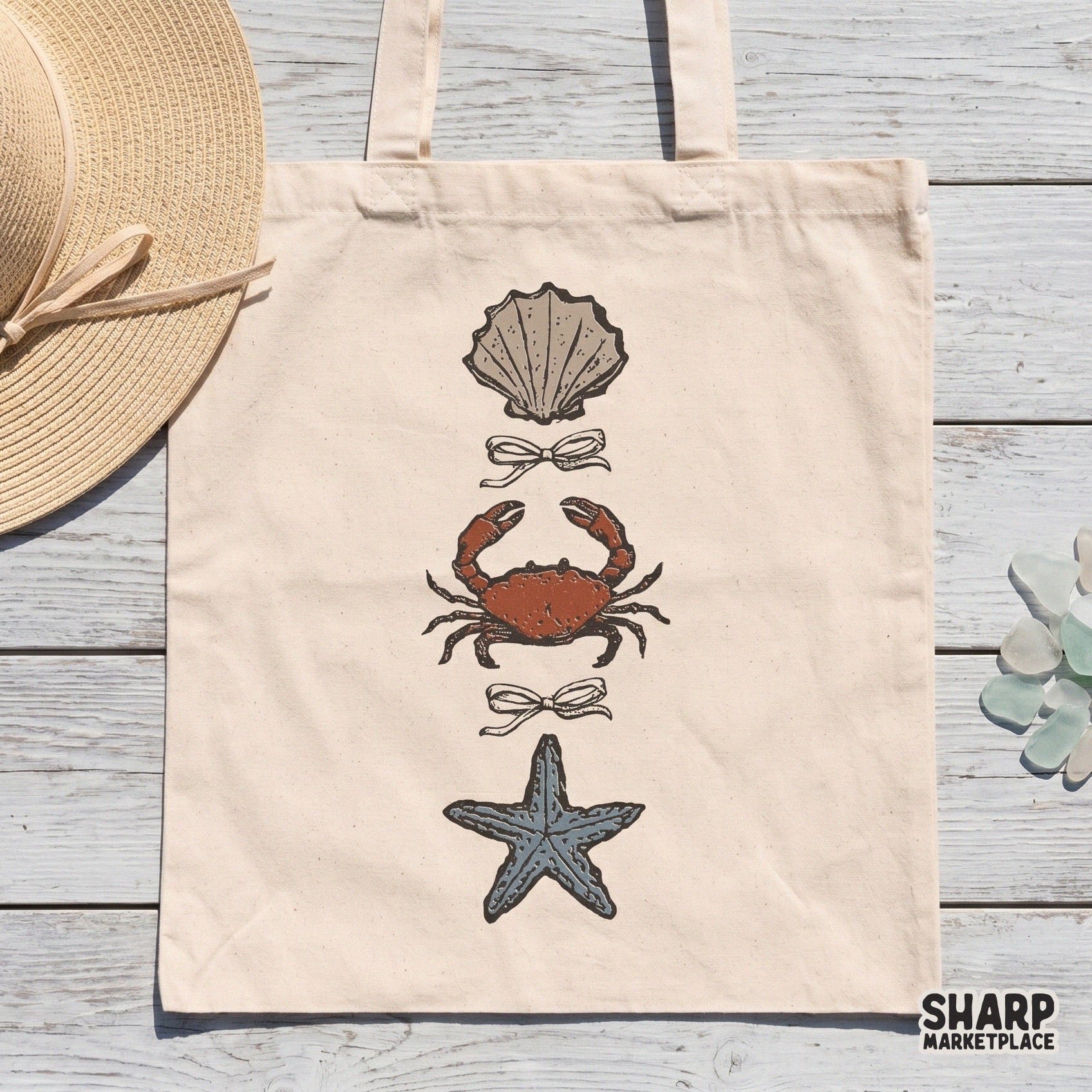 Digital sublimation design on a tote bag mockup showing a hand-drawn trio of a seashell, crab, and starfish with bows in a retro linocut style.