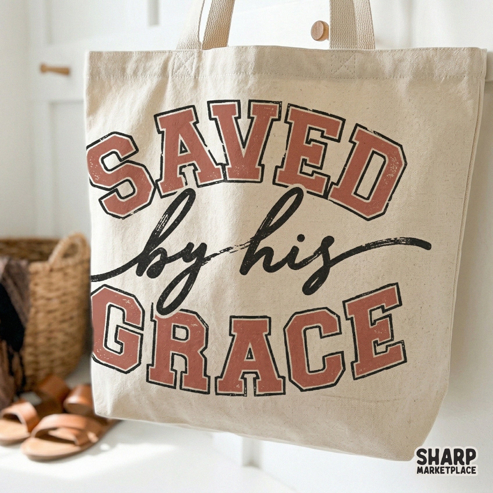 Tote bag mockup displaying the Saved By His Grace digital design with vintage athletic typography and a hand-drawn script aesthetic.