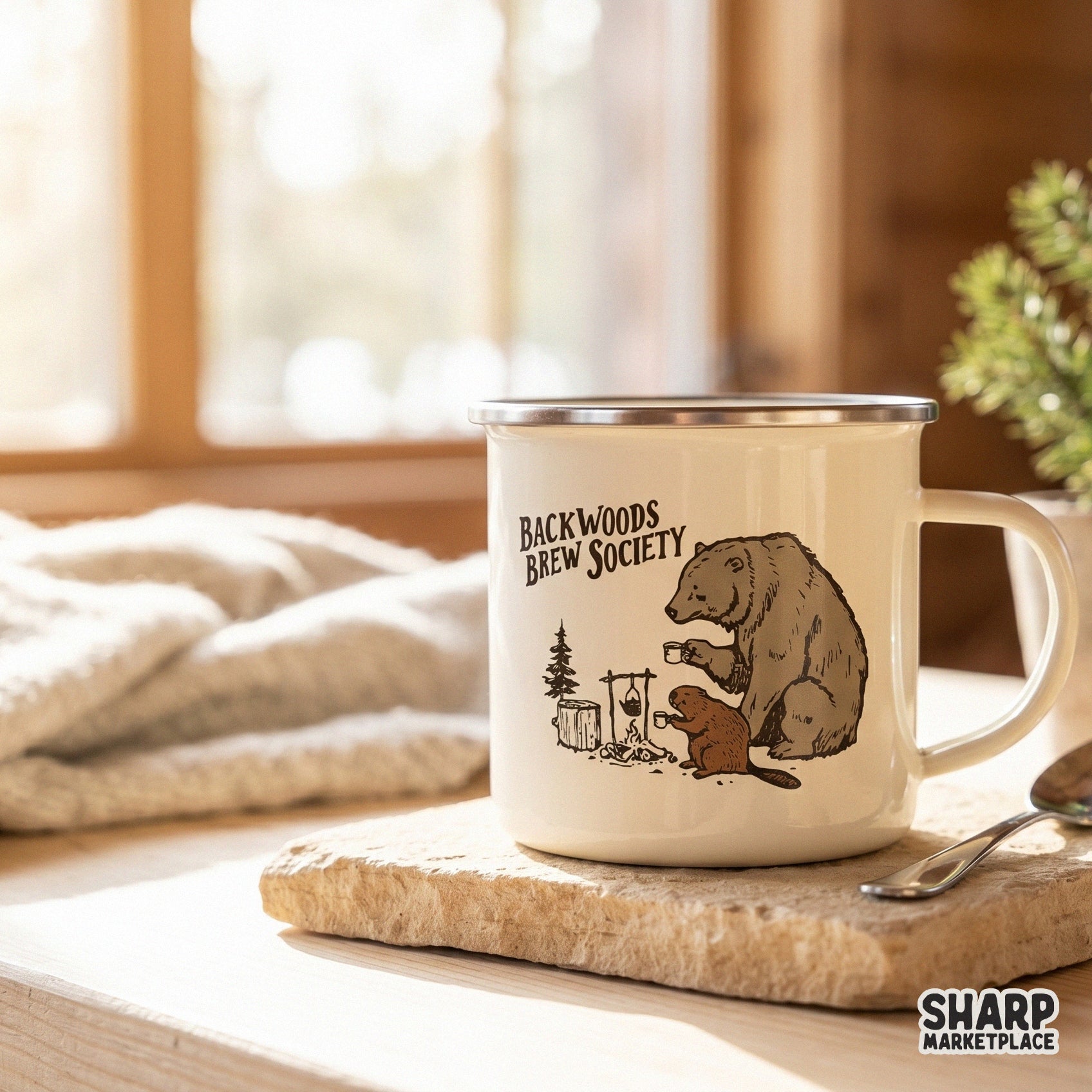 Cream-colored camping mug featuring a rustic illustration of a bear and beaver sharing coffee by a fire with Backwoods Brew Society text.