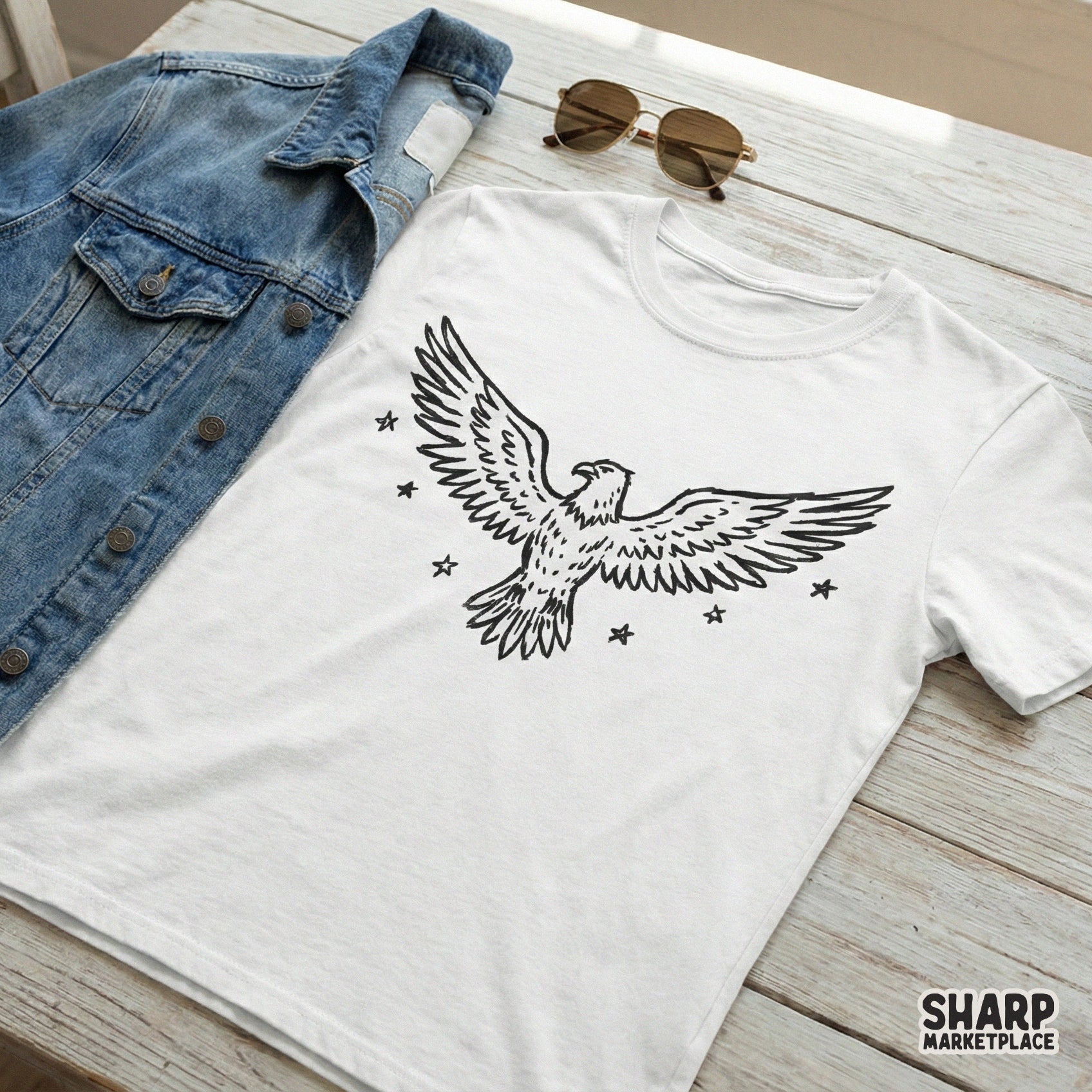 A white t-shirt mockup featuring a minimalist black line art eagle with wings spread wide and surrounding stars, ideal for custom clothing and sublimation.