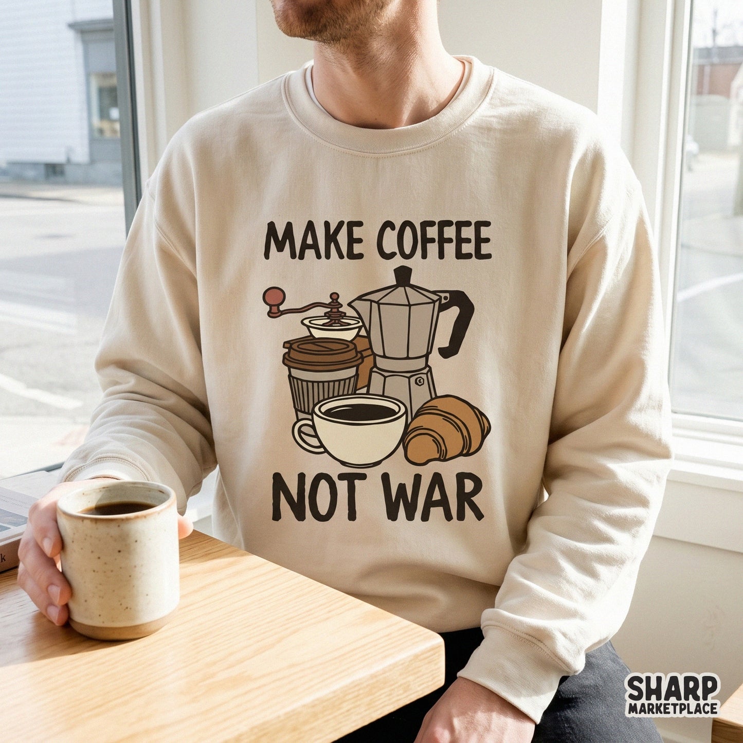 Cream-colored sweatshirt featuring a vintage-style cafe graphic with a moka pot, coffee cup, and croissant, captioned Make Coffee Not War.