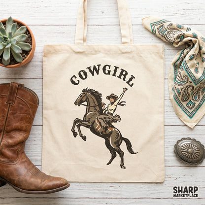 Trendy western apparel design featuring a cowgirl on a rearing horse with arched typography, displayed as a digital graphic on a canvas tote bag.